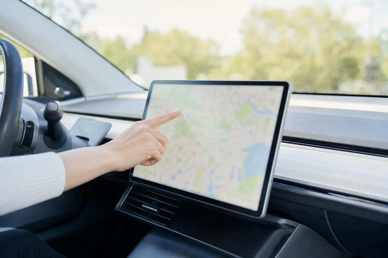 Driver's finger on a car infotainment screen showing a blurred map before selling the car