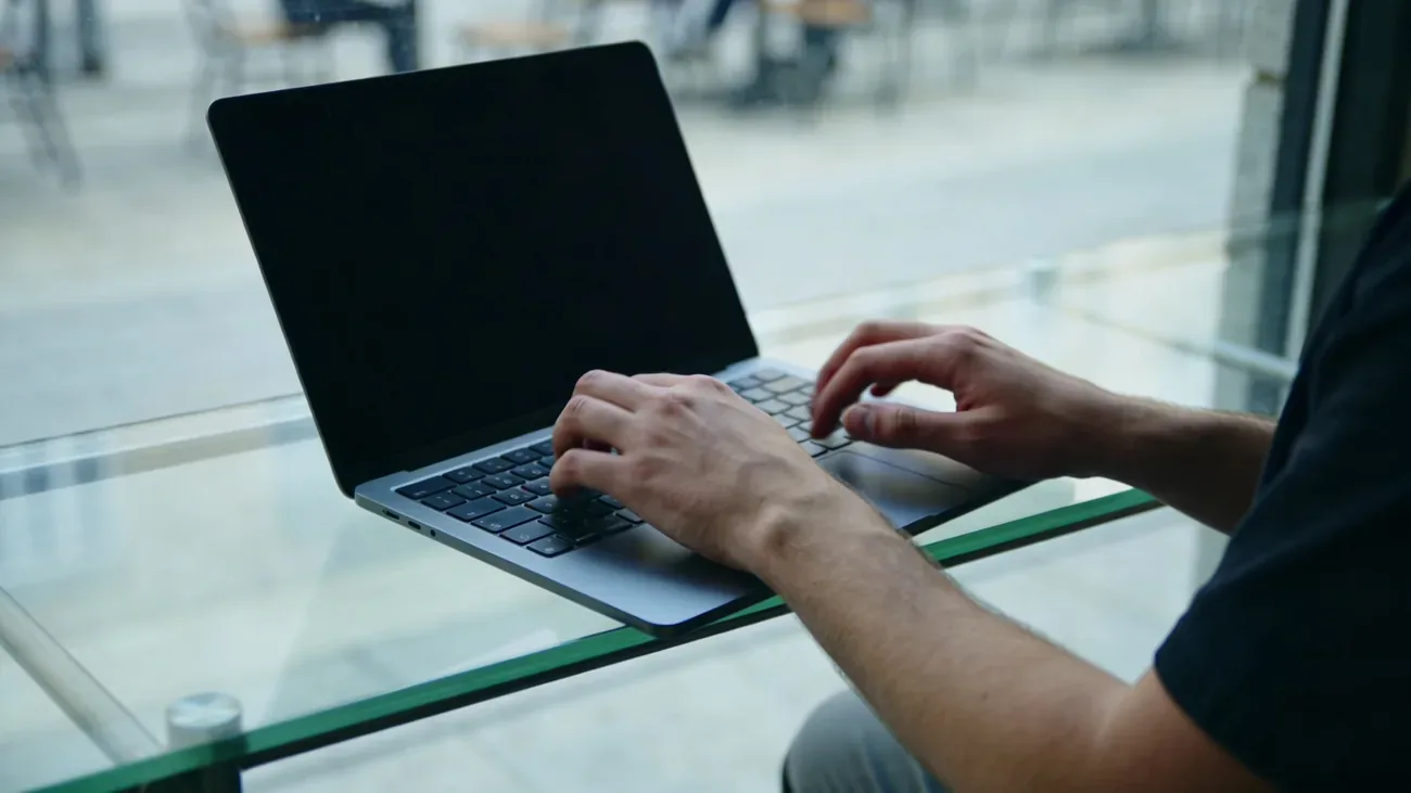 A pair of hands typing fast on a borrowed laptop in soft cool light, urgent posture