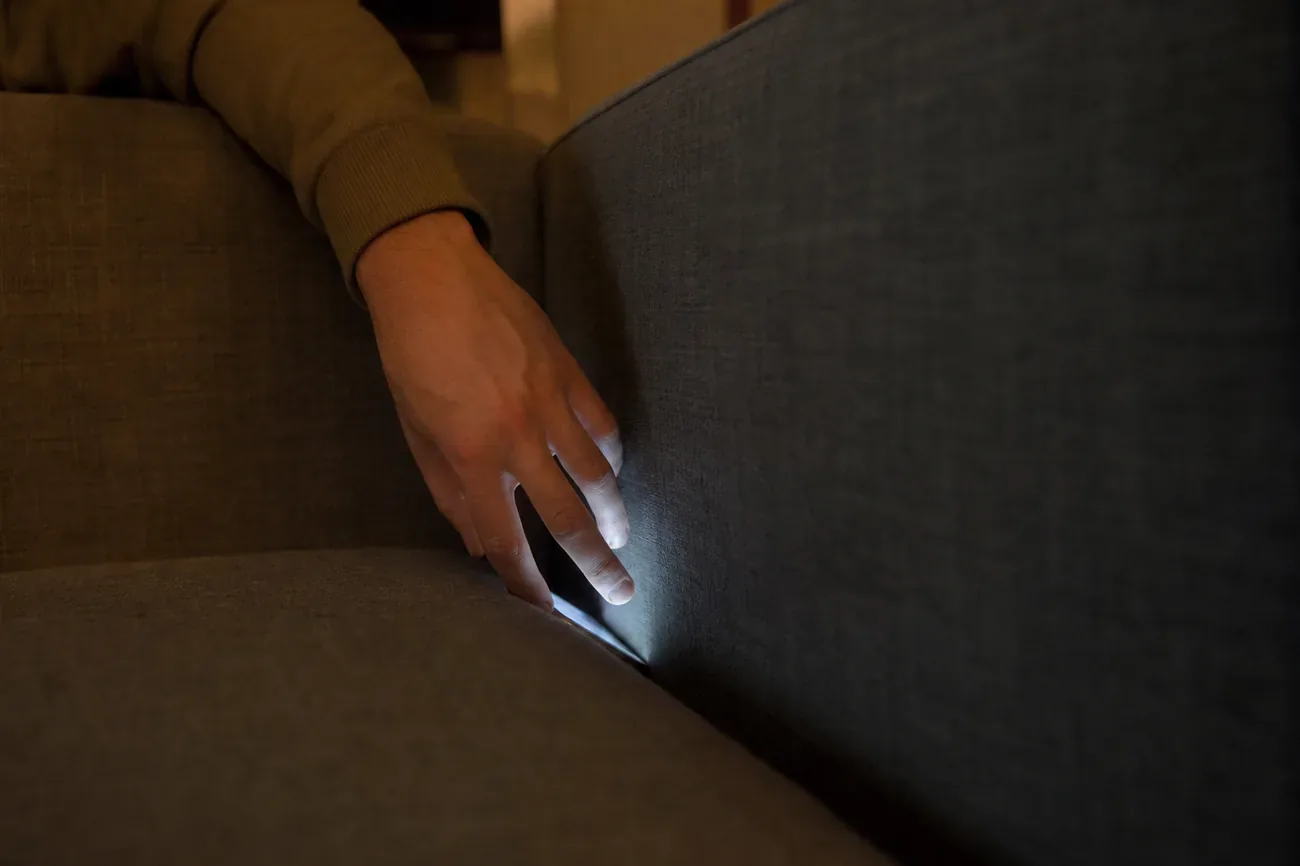 Điện thoại thông minh úp màn hình nằm giữa khe đệm ghế sofa, ánh sáng phòng khách dịu vào buổi chiều